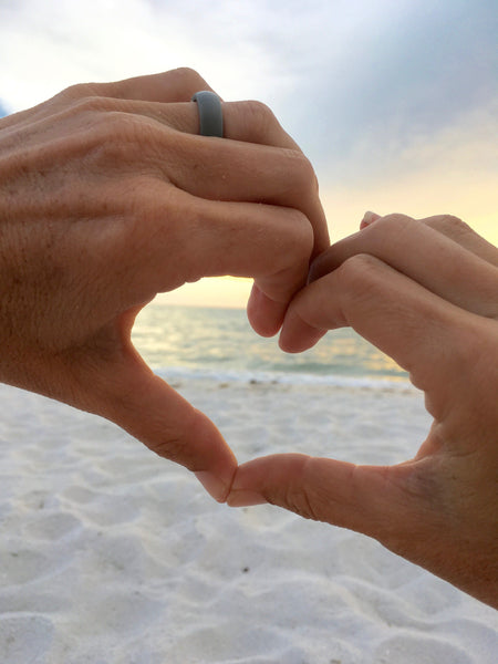 lady with hands forming a heart shape on the beach at sunset with grey silicone wedding ring on left finger