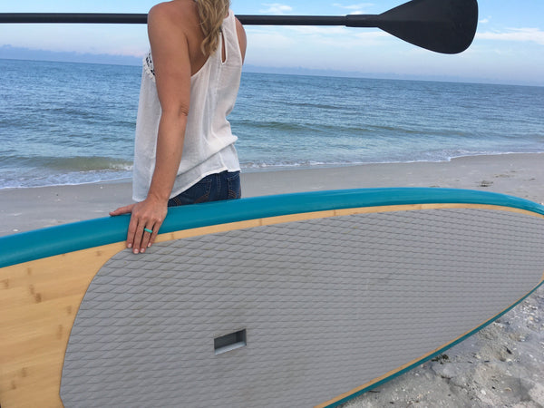 lady holding a paddle and paddleboard with teal silicone wedding ring on the beach with white tanktop