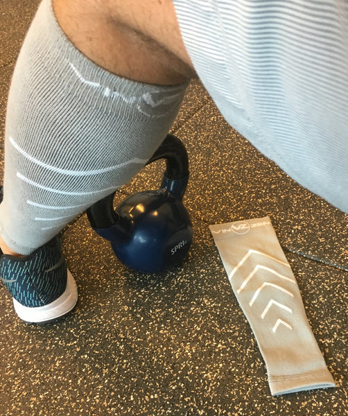 Grey compression calf sleeves on a man next to kettle bell in the gym xompression socks with no foot only for calves and shins